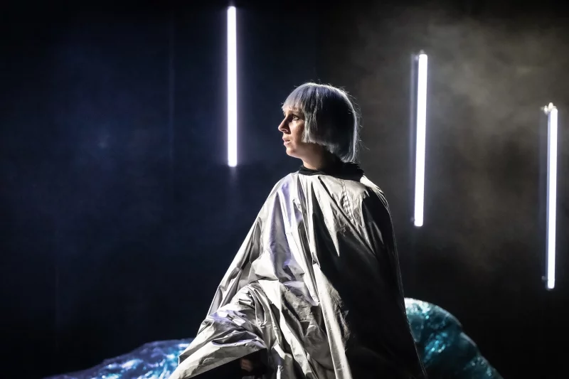 Eine Dame mit weißer Perrücke und silbernem Outfit sitzt enttäuscht auf der Bühne im dunklen Licht. | © Sandra Then